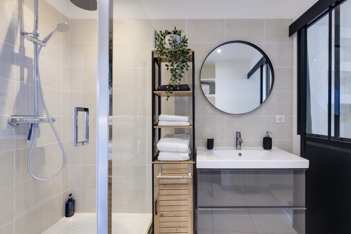 Salle de bain Herriot 5 Brive – Douche à l’italienne, meuble vasque gris, miroir rond et rangements en bois