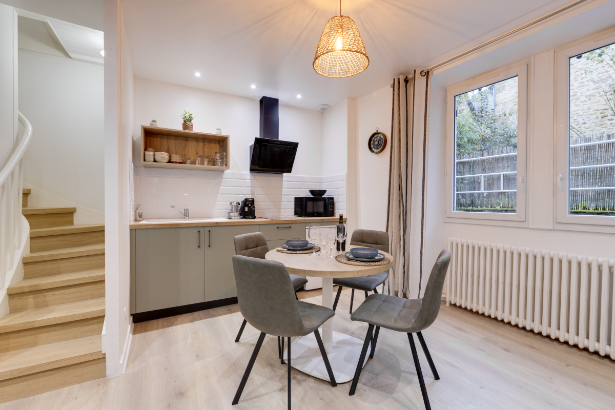 Cuisine équipée moderne avec espace repas pour quatre personnes, table ronde et chaises confortables dans un appartement rénové au cœur historique de Sarlat-la-Canéda.