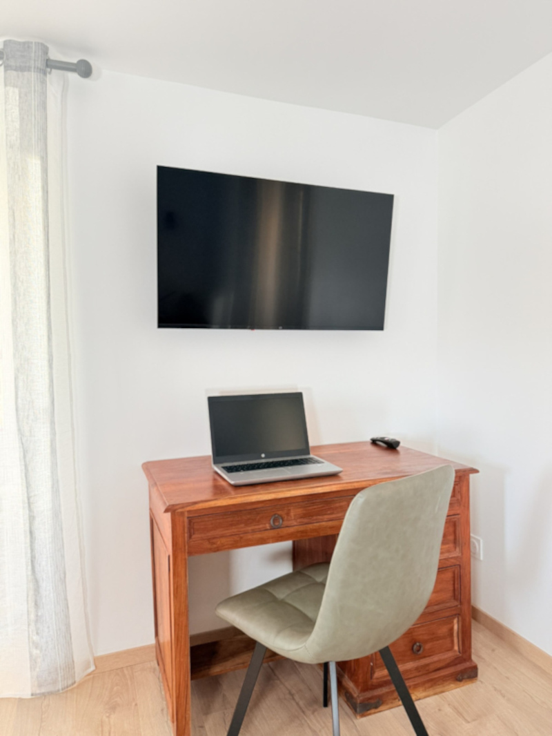 Espace bureau avec bureau en bois, écran mural et chaise confortable, idéal pour le télétravail – Appart’Cosy